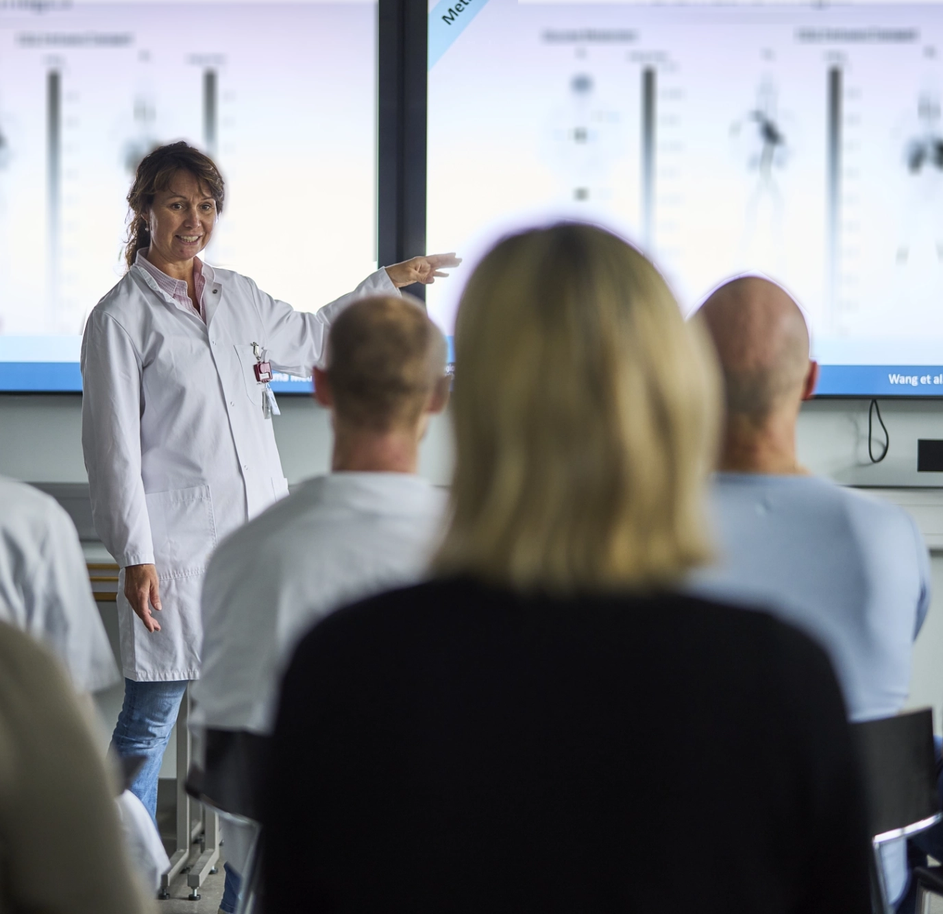 Lecturer comparing scans in front of two large screens
